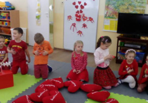 Kilkoro dzieci siedzących na piankowym dywanie. Przed nimi widać poduszki w kształcie serc ułożone w wielkie serce.